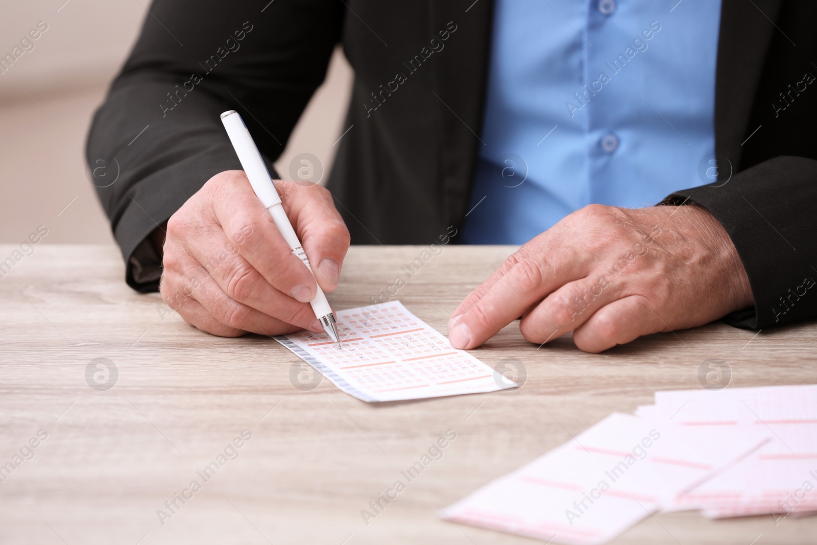 Photo of Senior man filling out lottery ticket at table, closeup