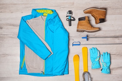 Flat lay composition with clothes, boots and skis on wooden background. Winter vacation