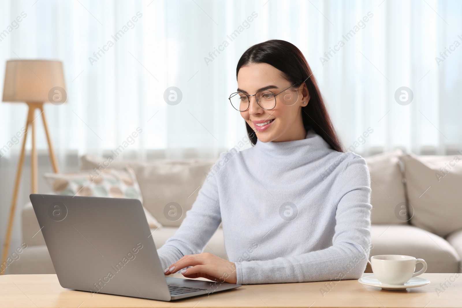 Photo of Happy woman working with laptop at wooden desk in room