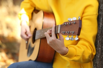 Photo of Teen girl playing guitar in autumn park, closeup