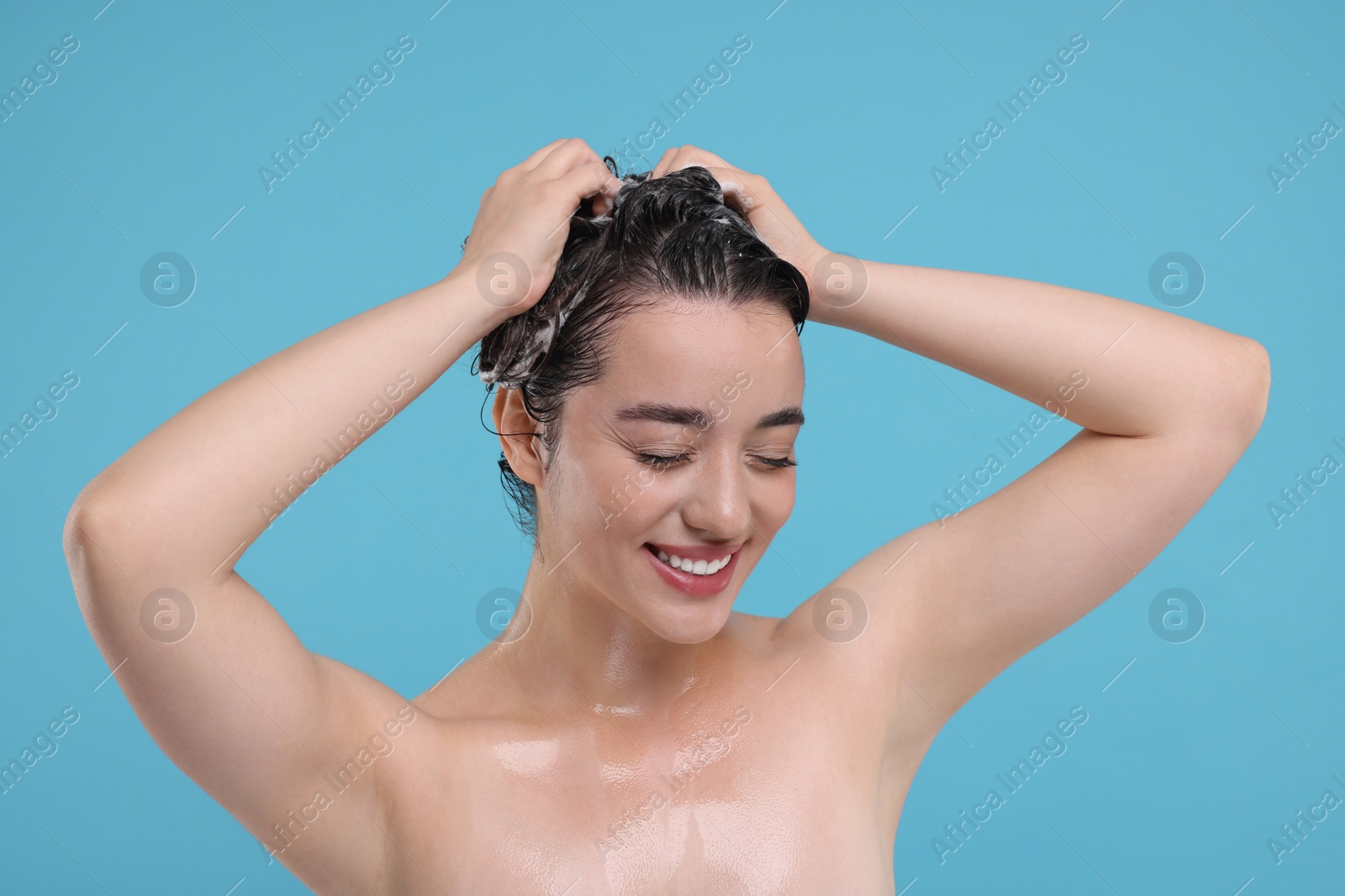 Photo of Portrait of beautiful happy woman washing hair on light blue background