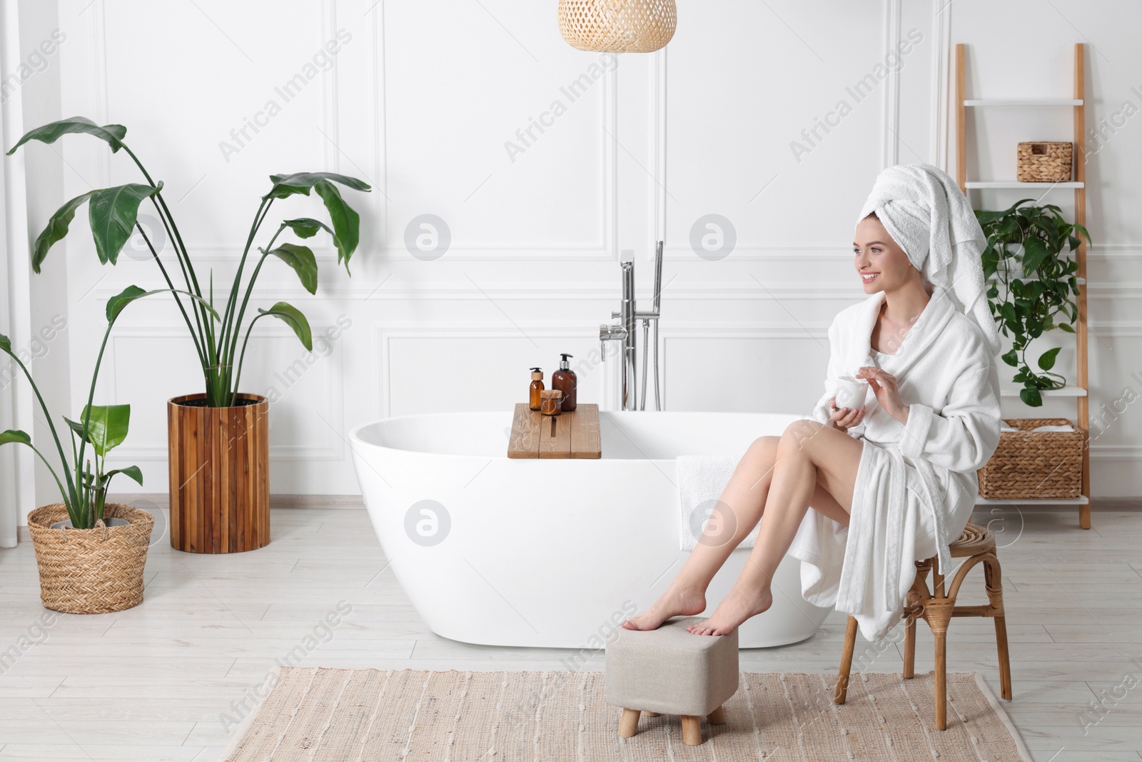 Photo of Beautiful young woman with body cream in bathroom, space for text