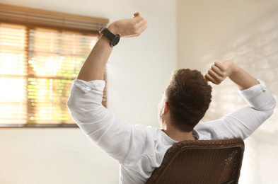 Photo of Young man relaxing near window at home, back view