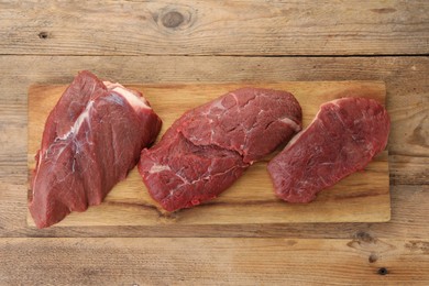 Photo of Pieces of raw beef meat on wooden table, top view