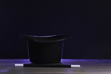 Photo of Magician's hat and wand on wooden table against black background, space for text