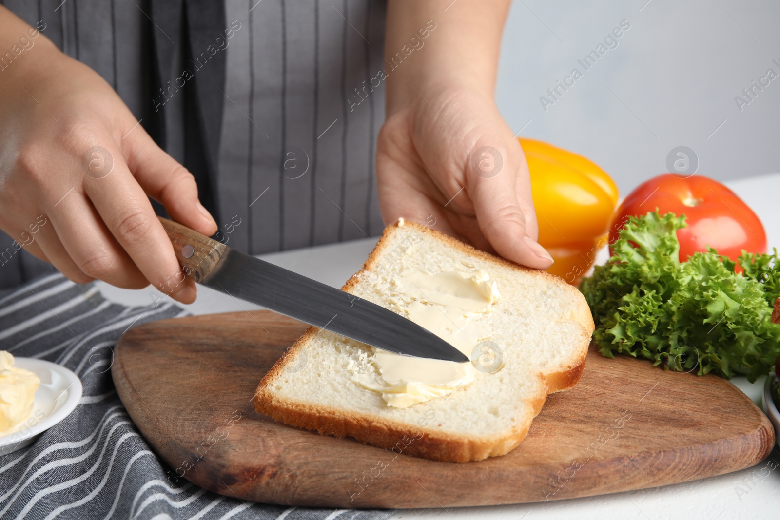 Photo of Woman spreading butter on sandwich at white table, closeup