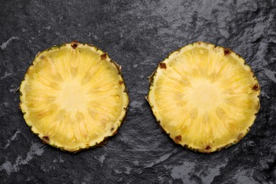 Photo of Slices of tasty ripe pineapple on black textured table, flat lay