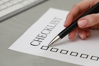 Woman filling Checklist at light grey table, closeup