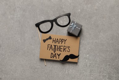 Photo of Card with phrase Happy Father's Day, gift box and paper glasses on grey background, flat lay
