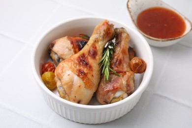 Photo of Marinade, roasted chicken drumsticks, rosemary and tomatoes on white tiled table, closeup