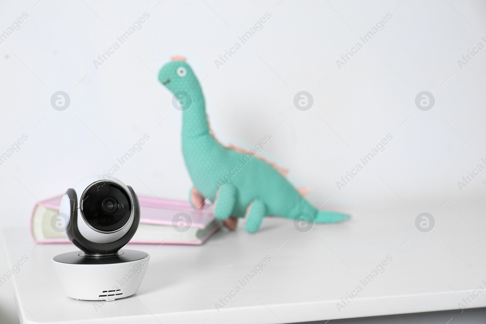 Photo of Baby camera with toy and photo album on table against white background, space for text. Video nanny