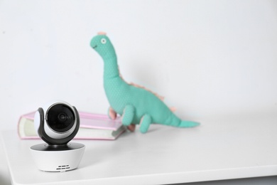 Photo of Baby camera with toy and photo album on table against white background, space for text. Video nanny