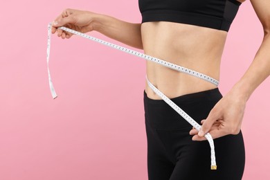 Photo of Slim woman measuring waist with tape on pink background, closeup and space for text. Weight loss