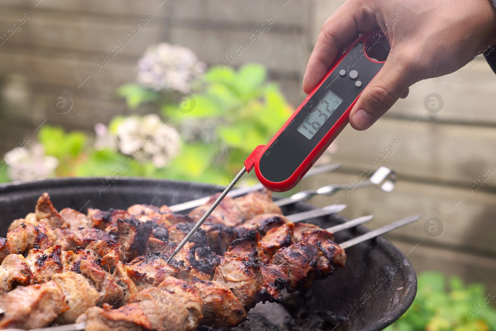 Photo of Man measuring temperature of delicious kebab on metal brazier outdoors, closeup