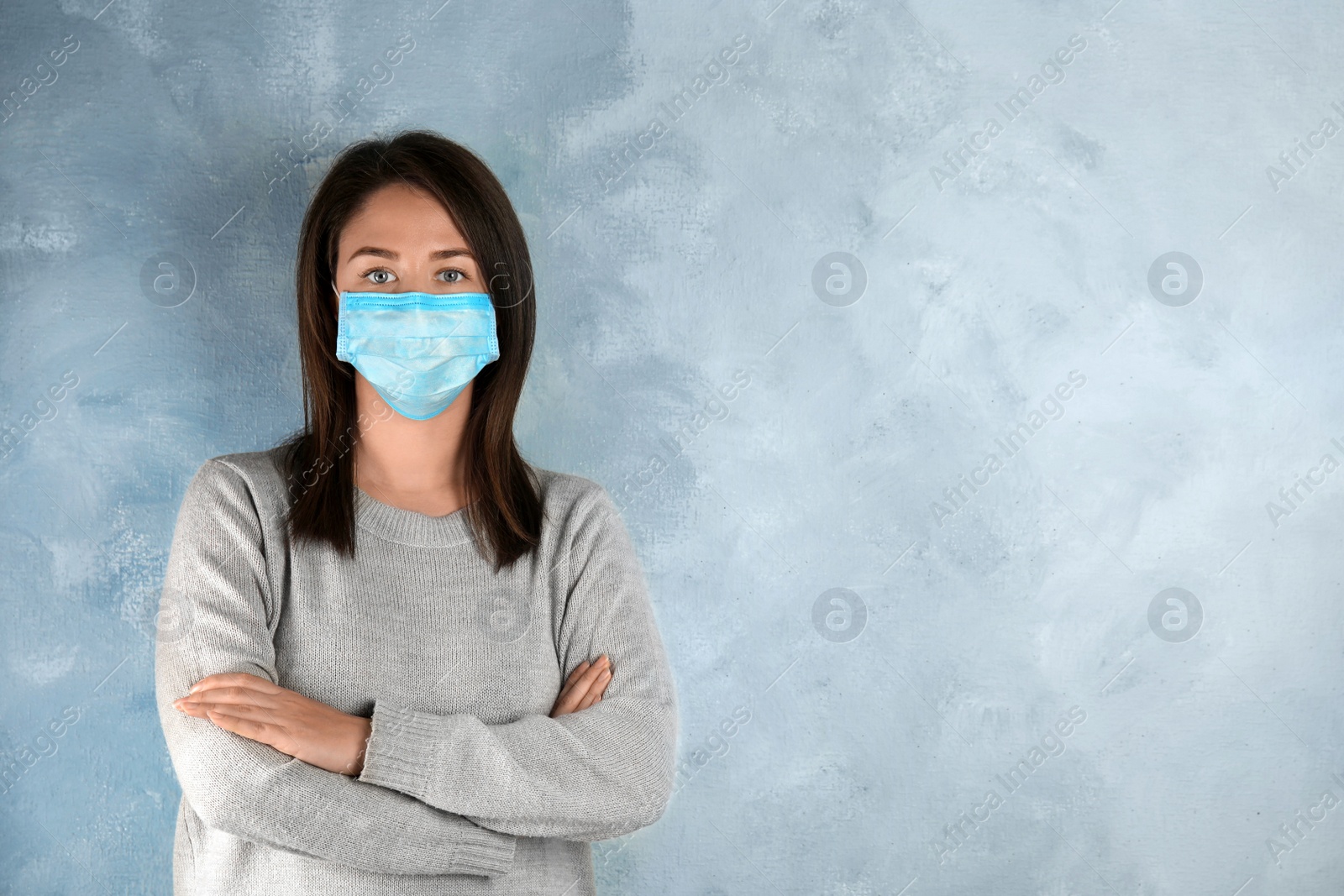 Photo of Woman with disposable mask on face against light blue background. Space for text