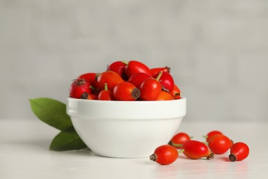 Ripe rose hip berries with green leaves on white wooden table