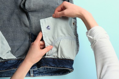 Woman holding jeans with ink stain on light blue background, top view