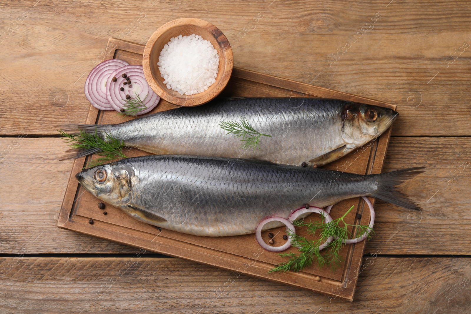 Photo of Board with delicious salted herrings, dill, onion and salt on wooden table, flat lay