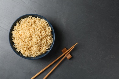 Photo of Bowl with tasty instant noodles and chopsticks on table, flat lay. Space for text