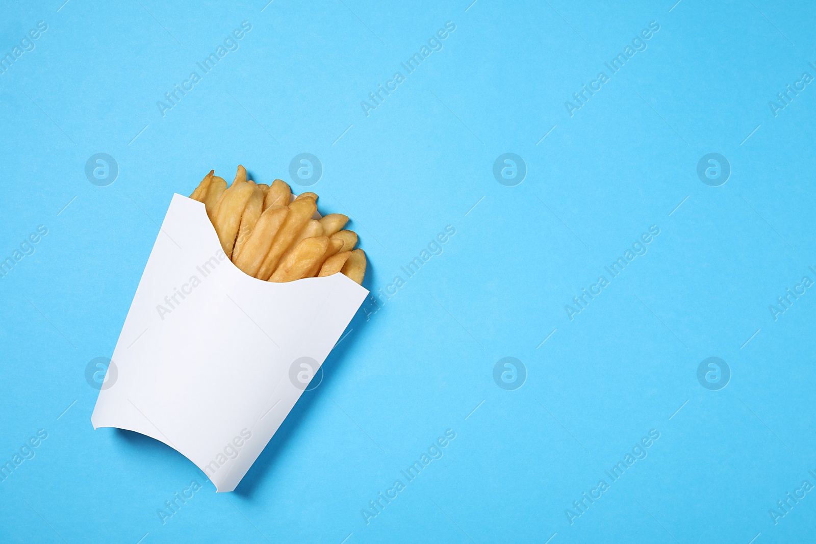 Photo of Paper cup with French fries on light blue table, top view. Space for text