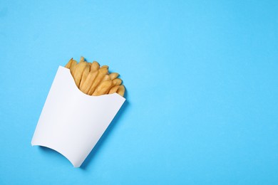 Paper cup with French fries on light blue table, top view. Space for text