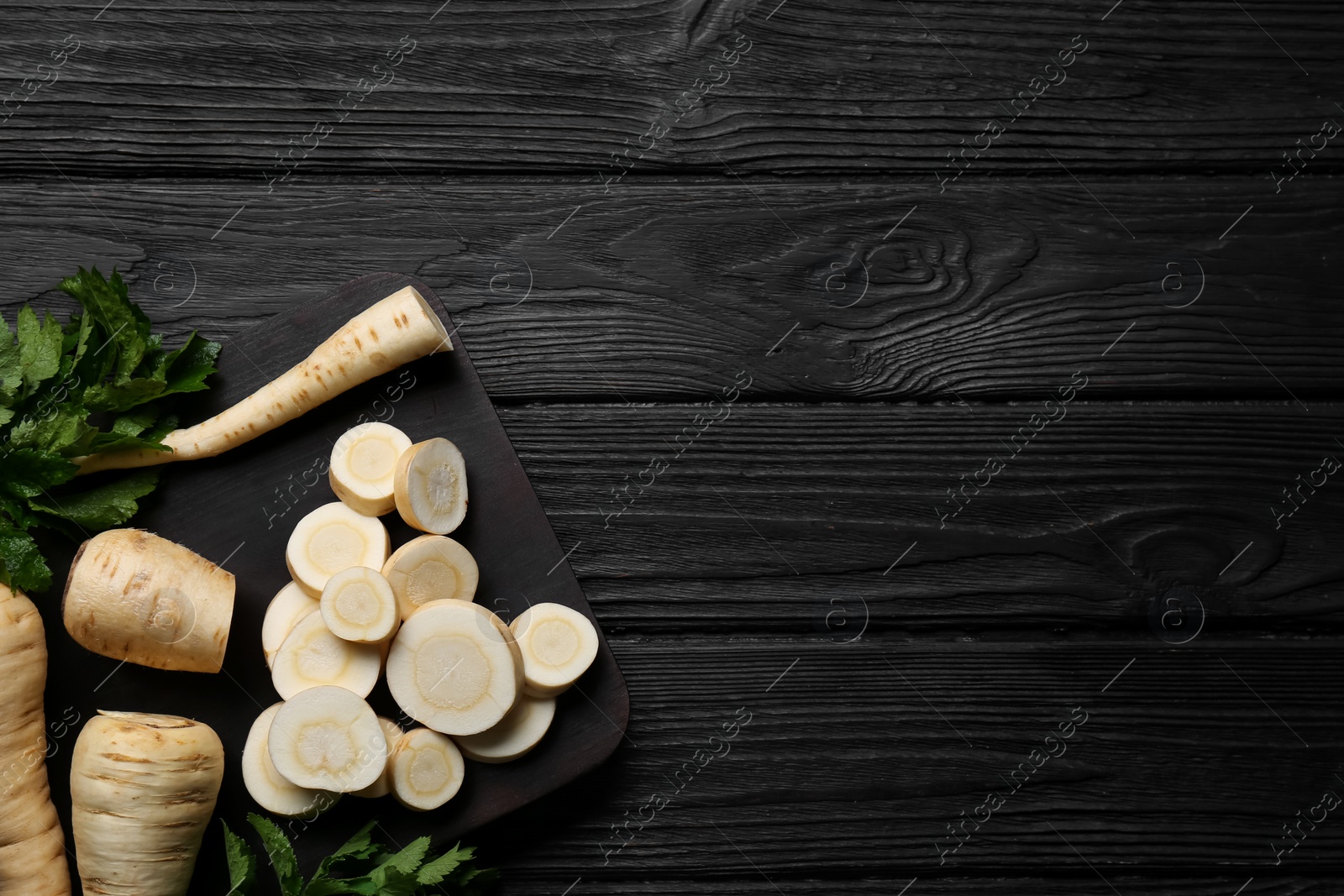 Photo of Whole and cut parsnips on black wooden table, flat lay. Space for text