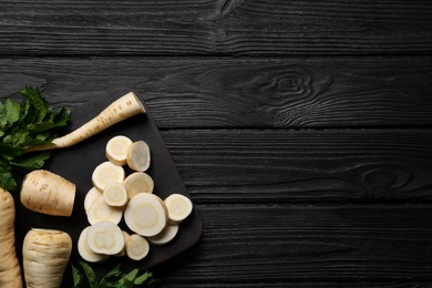 Photo of Whole and cut parsnips on black wooden table, flat lay. Space for text