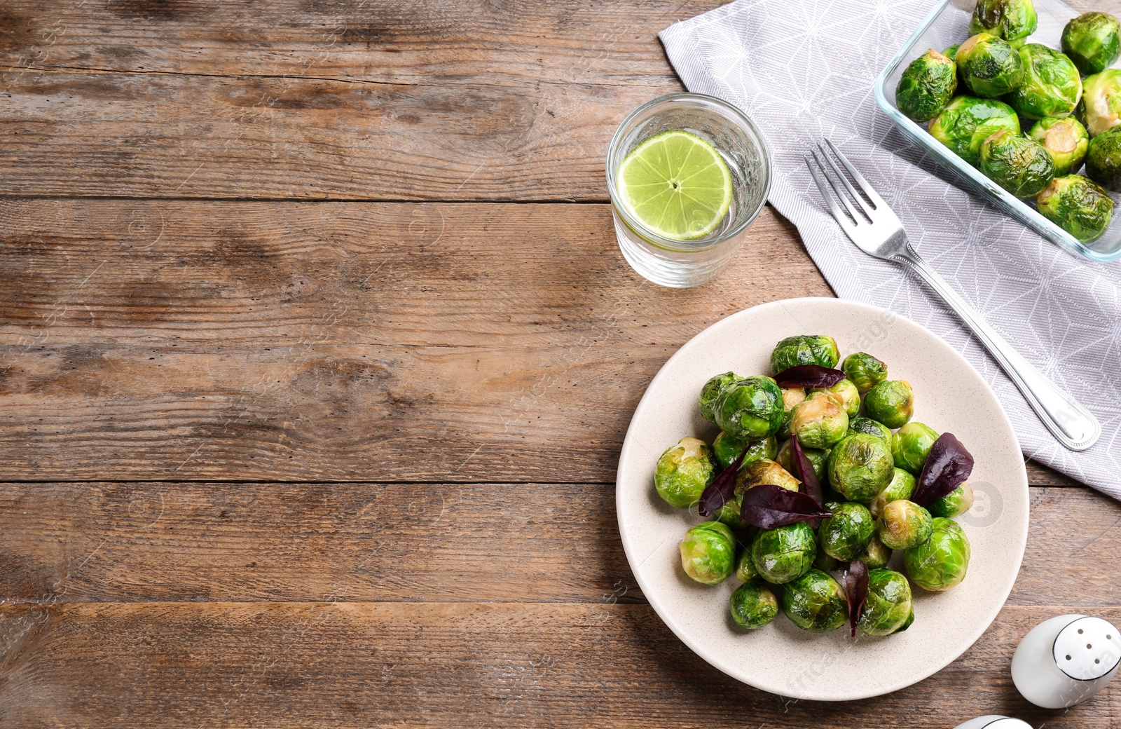 Photo of Roasted Brussels sprouts and water with lime served on wooden table, flat lay. Space for text