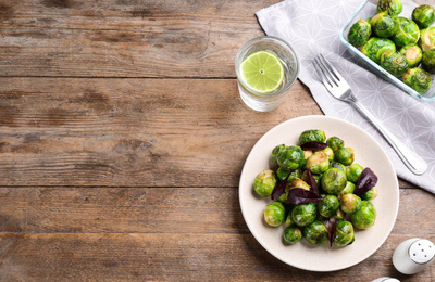 Photo of Roasted Brussels sprouts and water with lime served on wooden table, flat lay. Space for text