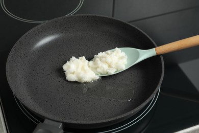 Photo of Frying pan with coconut oil and spoon on induction stove, closeup. Healthy cooking