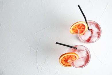 Glasses of drink with orange and ice cubes on white table, top view. Space for text