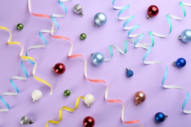 Colorful serpentine streamers and Christmas balls on violet background, flat lay