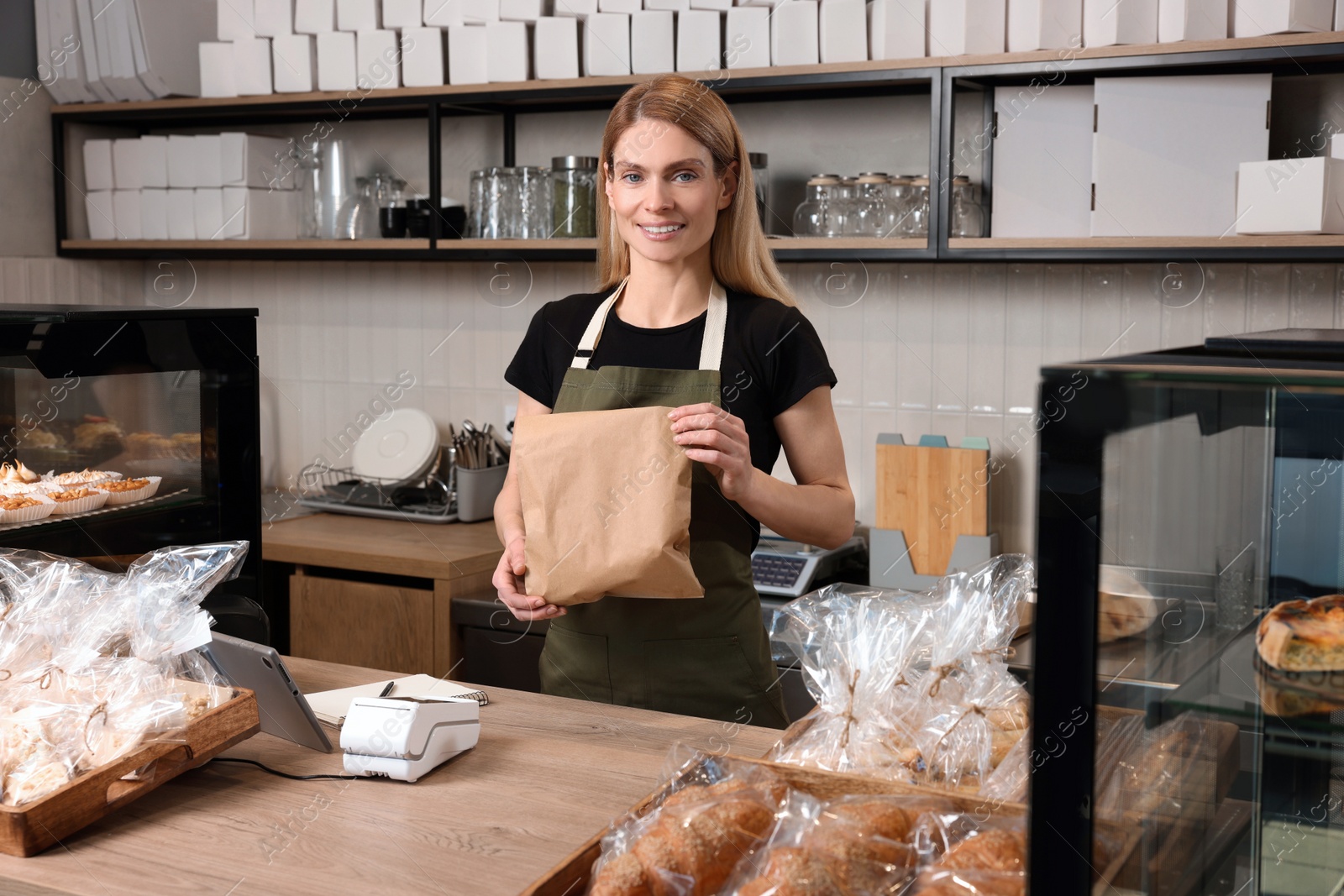 Photo of Happy seller with paper bag at cashier desk in bakery shop