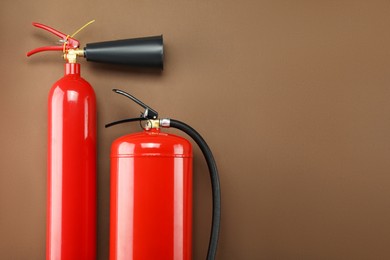 Photo of Fire extinguishers on brown background, flat lay. Space for text