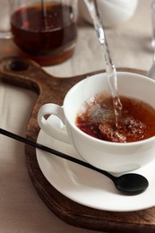 Photo of Pouring hot water into cup with tea bag on light table, closeup