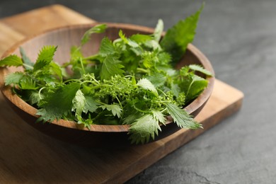 Fresh stinging nettle leaves in wooden bowl on black table, closeup