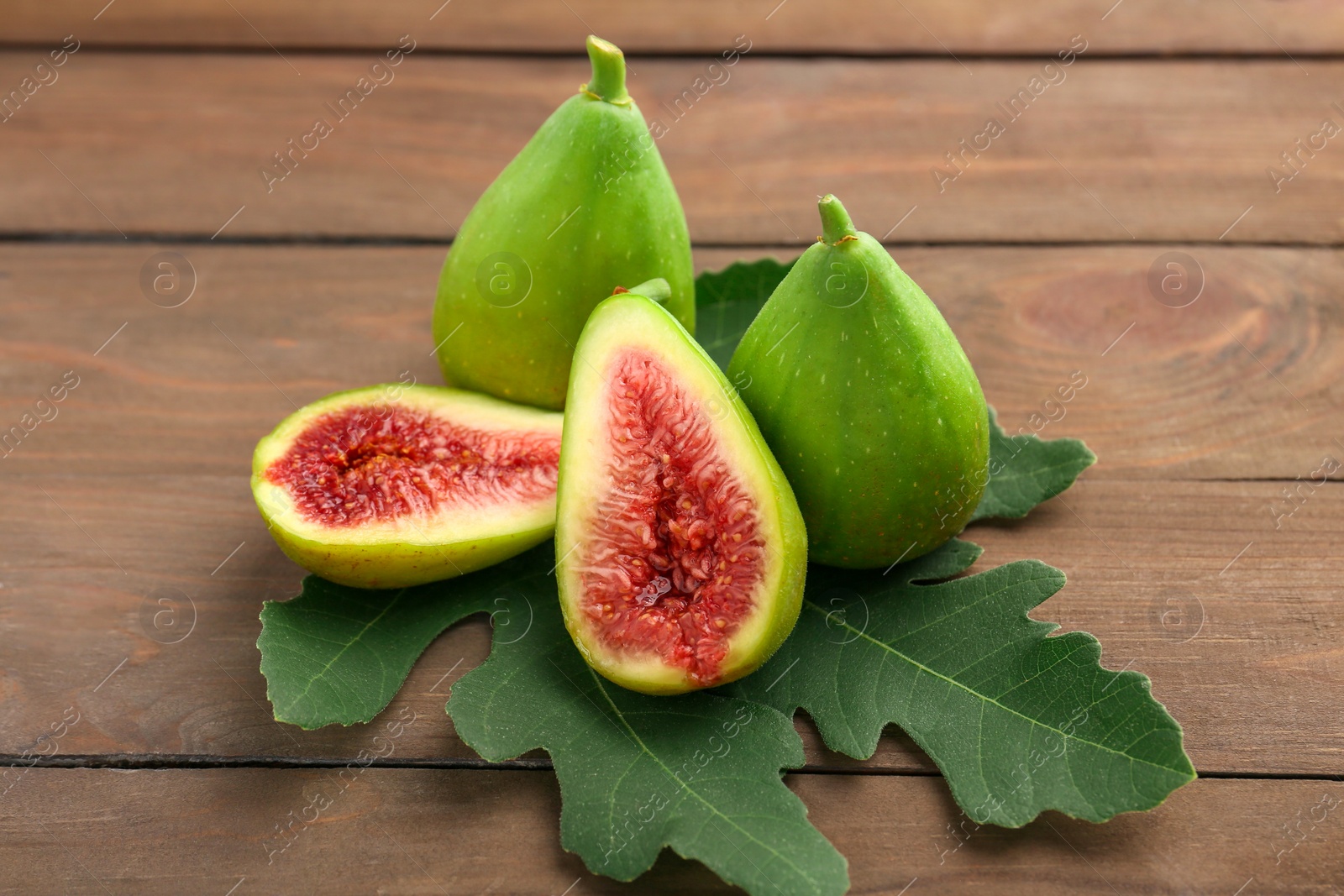 Photo of Cut and whole green figs on wooden table