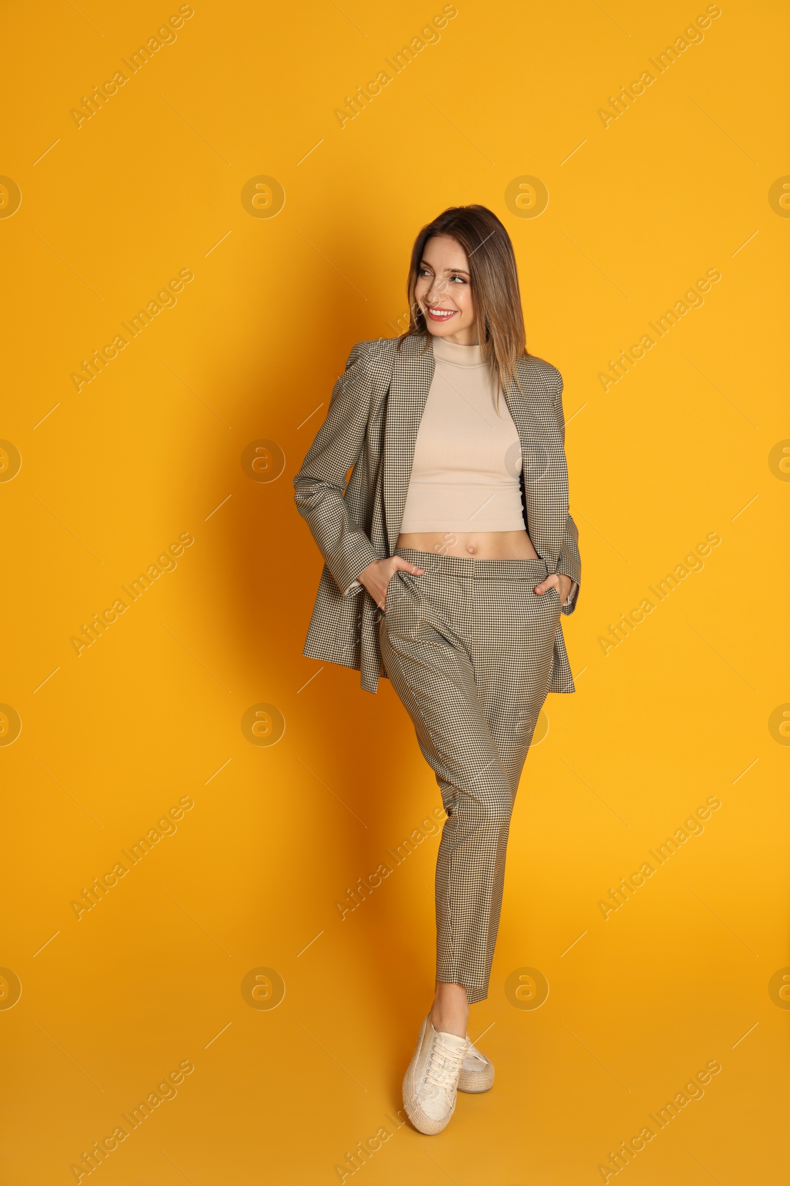 Photo of Full length portrait of beautiful young woman in fashionable suit on yellow background. Business attire