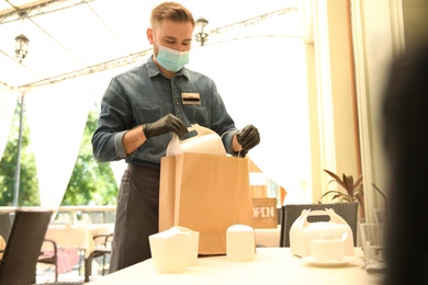 Photo of Waiter packing takeout order in restaurant. Food service during coronavirus quarantine