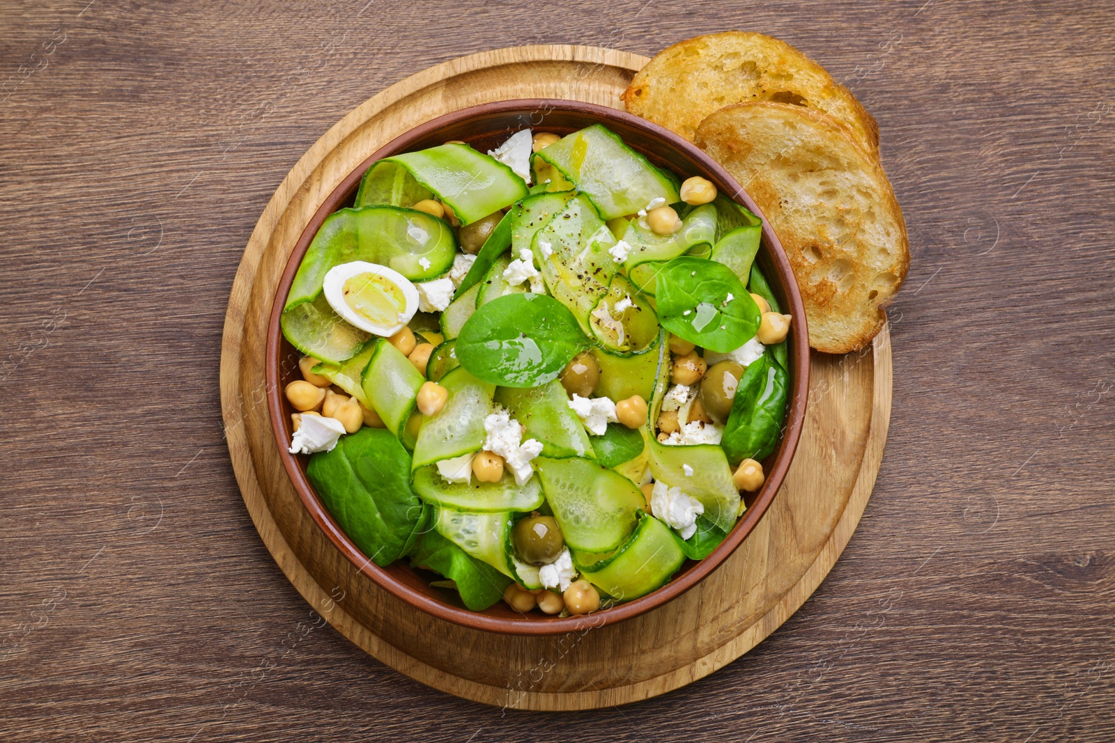 Photo of Bowl of delicious cucumber salad and toasted bread on wooden table, top view