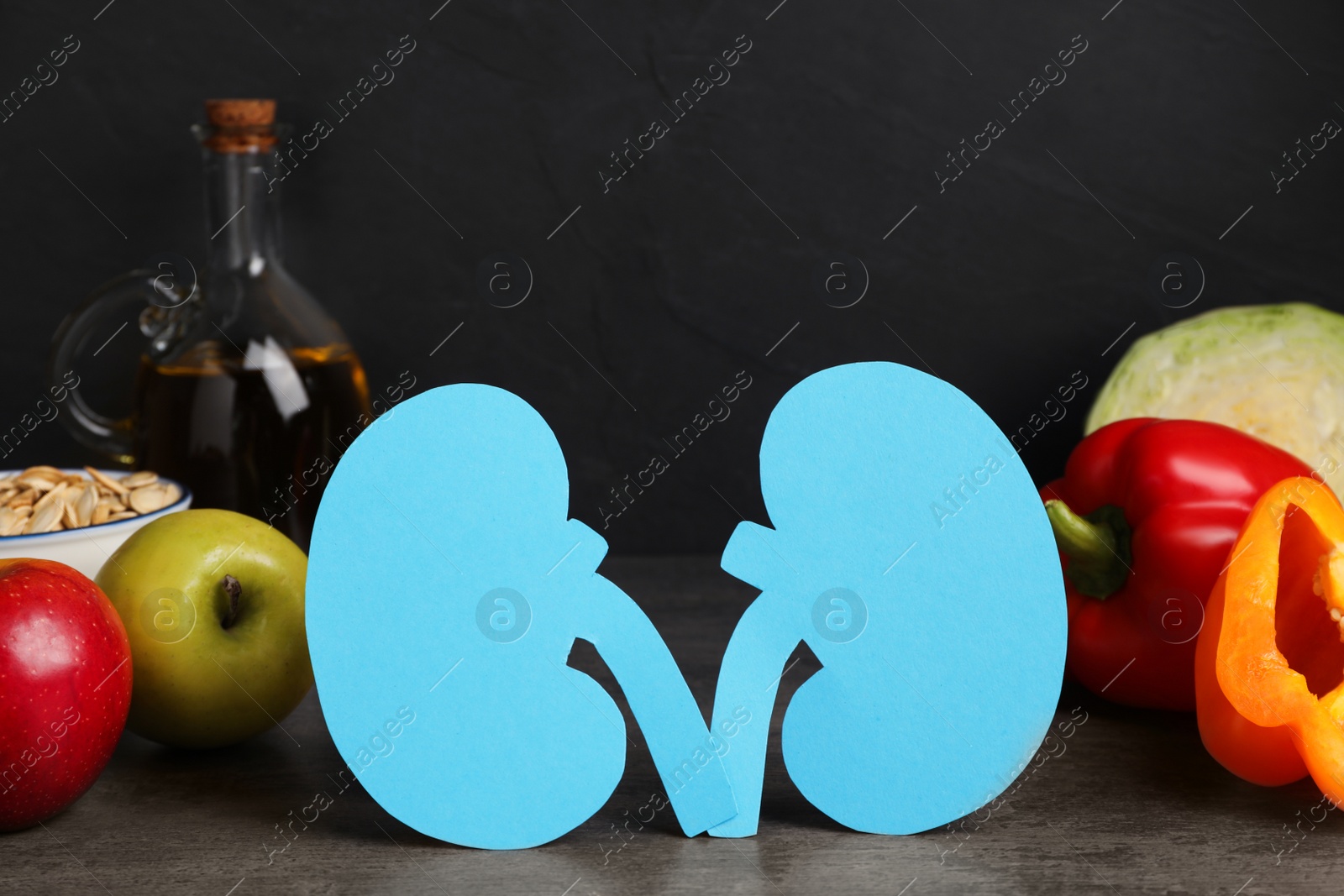 Photo of Paper cutout of kidneys and different products on grey table against dark background