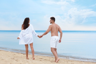 Happy young couple walking together on beach near sea