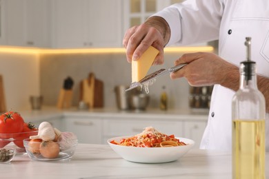 Photo of Professional chef grating cheese into delicious dish at white marble table indoors, closeup. Space for text