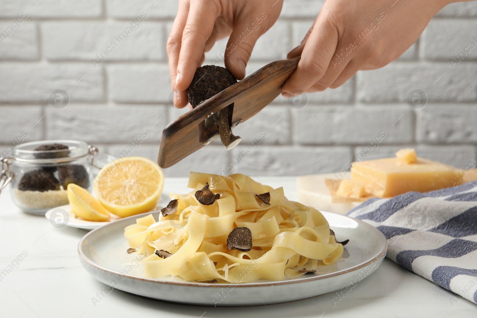 Photo of Woman slicing truffle over delicious pasta at white table, closeup