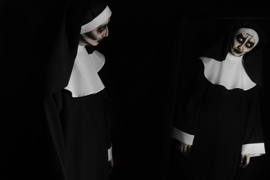Photo of Scary devilish nun near mirror on black background. Halloween party look