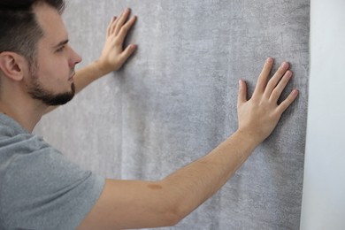 Photo of Man hanging stylish gray wallpaper in room