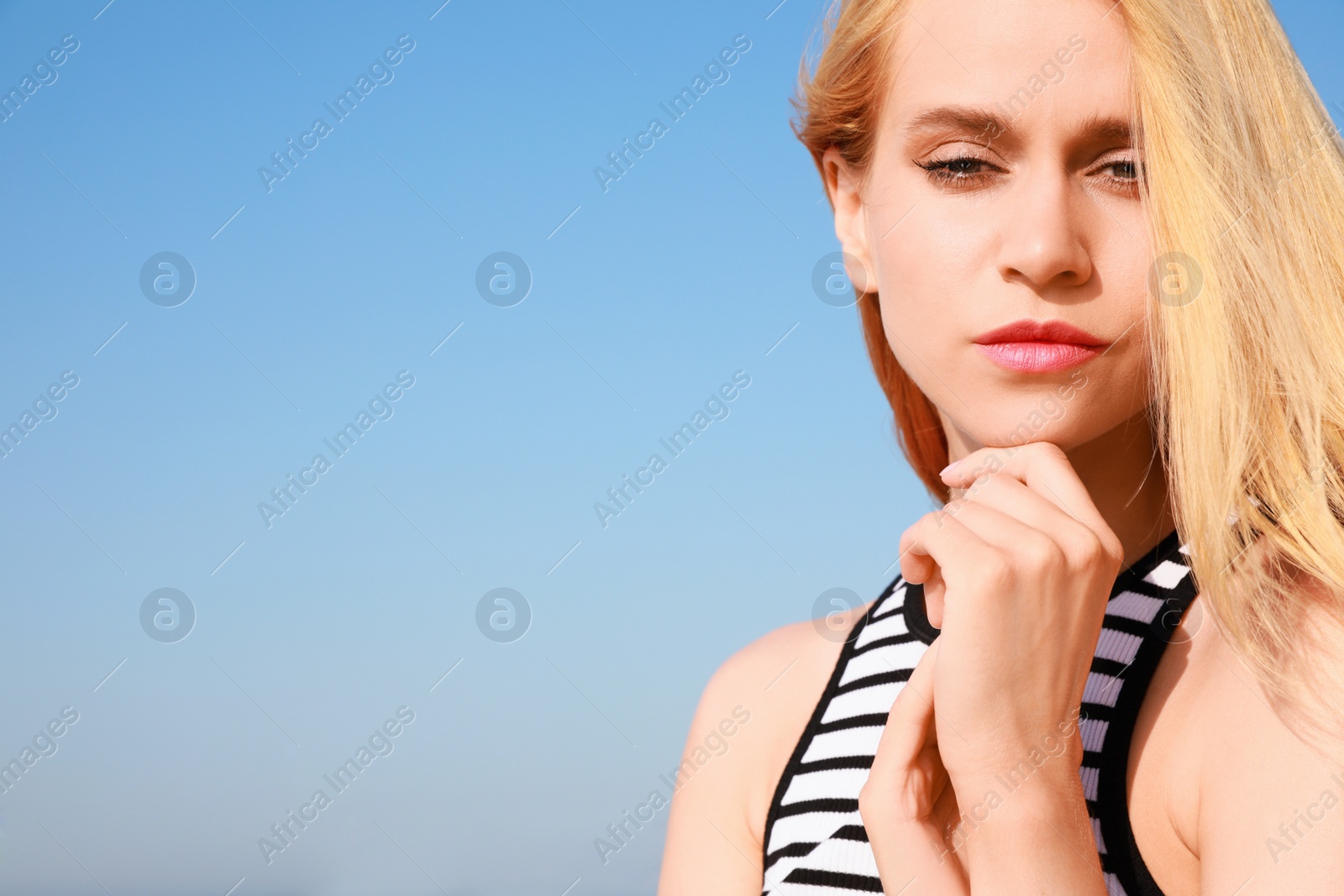 Photo of Beautiful young woman against blue sky on sunny day, closeup. Space for text