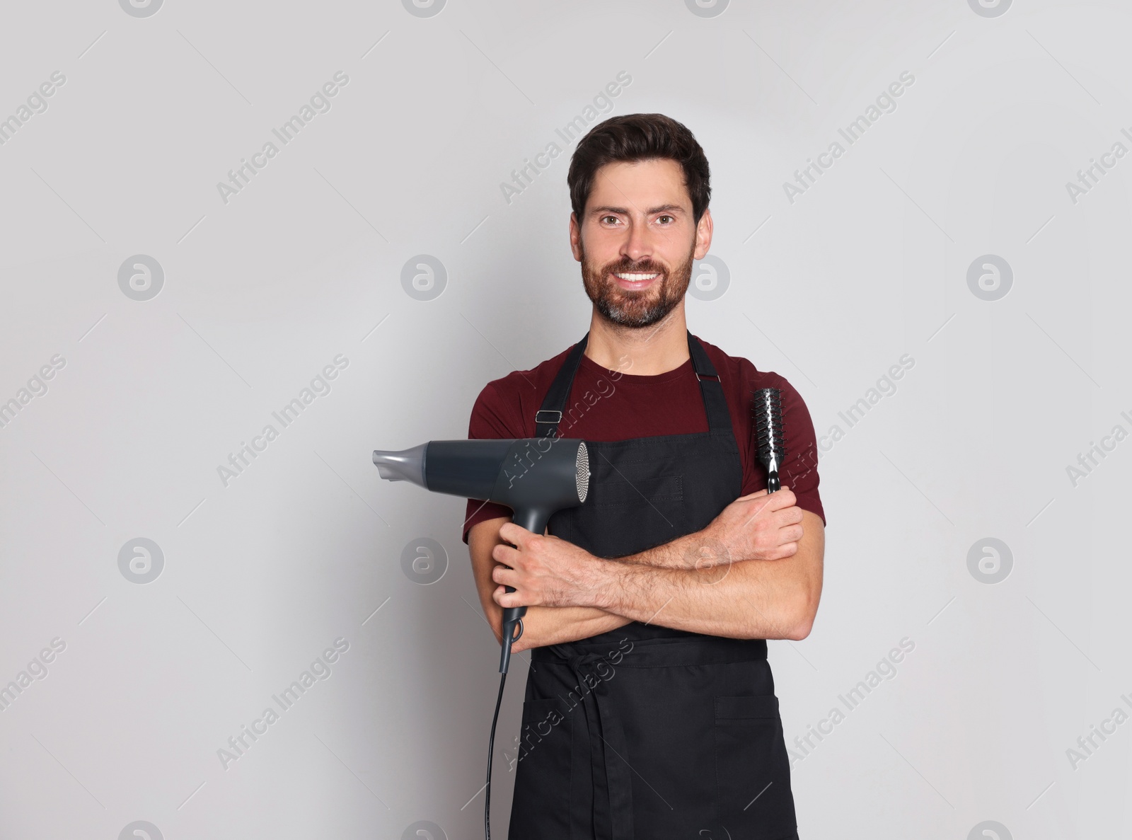 Photo of Smiling hairdresser with dryer and brush on light grey background