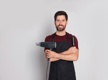 Smiling hairdresser with dryer and brush on light grey background