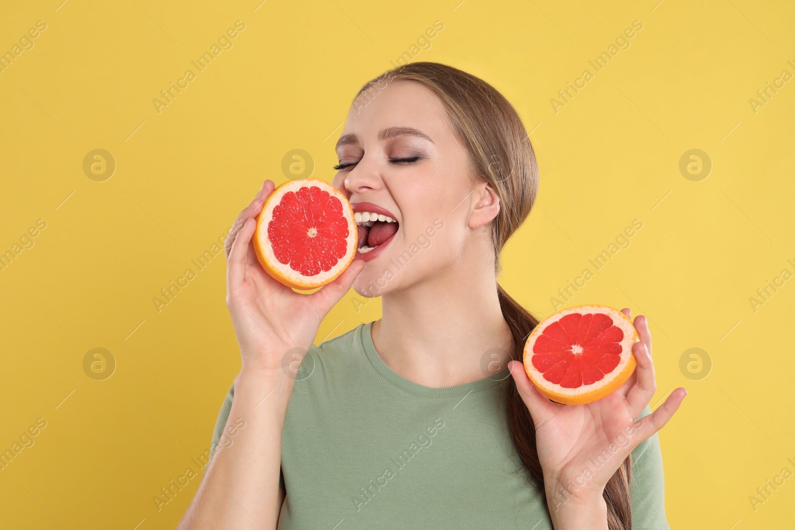 Photo of Emotional young woman with cut grapefruit on yellow background. Vitamin rich food